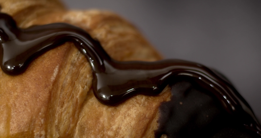 Dark chocolate is poured onto a French croissant with chocolate filling on a wooden table, small white delicious topping in topping. Super slow motion, 4K. Royalty-Free Stock Footage #1072725872
