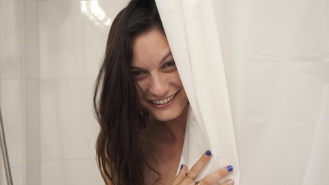 woman showering. peeking from behind shower curtains in the bathroom. cute naked sexy girl looking from the shower and smiling at  camera. Lady in shower. shy teasing gestures flirting with the camera