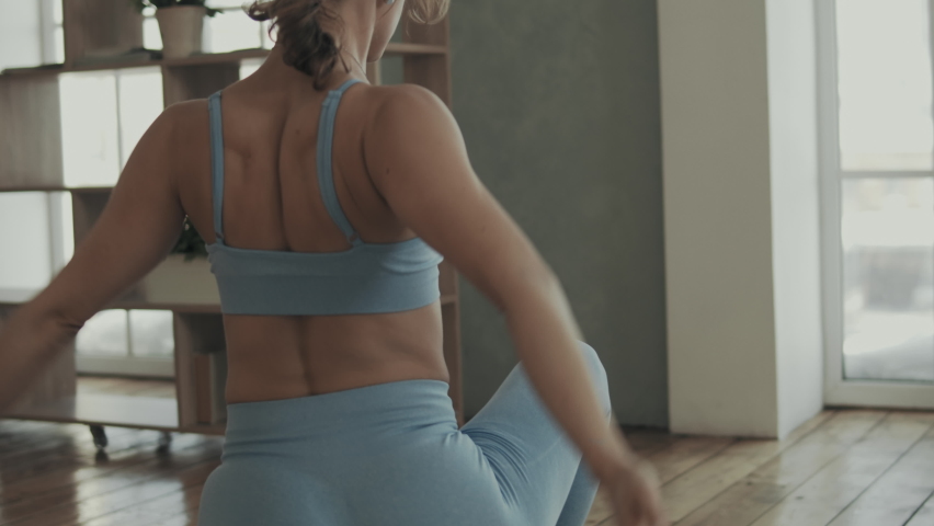 Rear view of young barefoot woman blue tight sportswear doing yoga excercise on yoga mat in her apartmanet at home