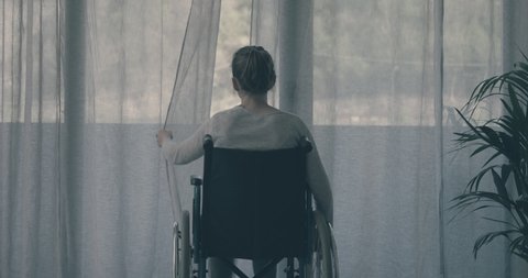 Disabled woman at home alone: she opens the curtain and looks outside