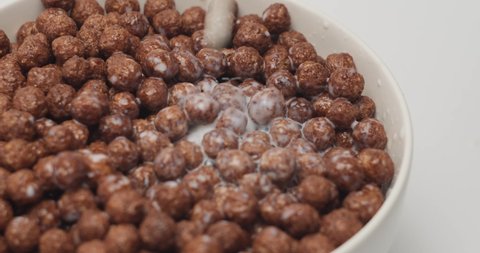 Milk is poured into a full white bowl with chocolate cereal balls