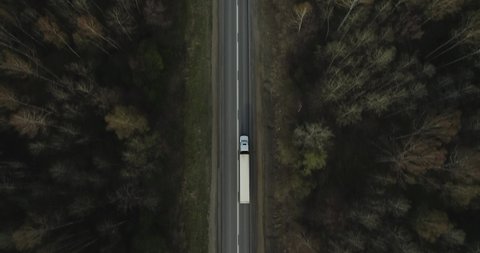 One Semi Truck with white trailer and cab driving, traveling alone on dense flat forest asphalt straight road, highway top down view follow vehicle aerial footage. Freeway trucks traffic