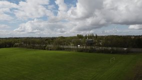 Aerial view of a sports field and a busy road with moving traffic in the background. 4K drone footage. 