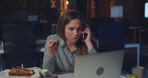 Dissapointed female office worker talking on phone with her boss , telling her to finish lot of work for tomorrow. Woman using laptop and having phone conversation at night office