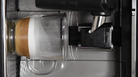 Modern home appliance coffee maker pouring hot espresso to prepare coffee with milk in transparent glass mug. Making cappuccino for breakfast