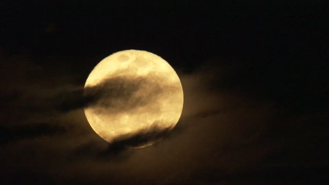 dark moody clouds crossing yellow moon reflecting the sun