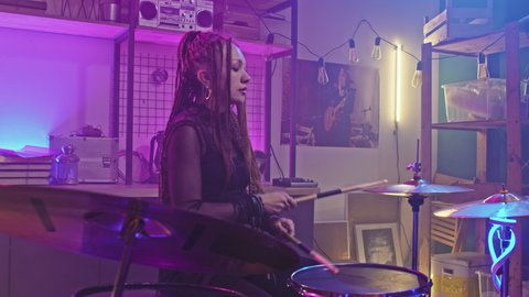Medium slowmo of cool rock-n-roll girl with dreadlocks and gothic makeup playing drums during rock concert at night club