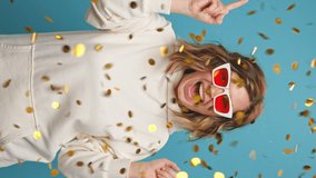 Party concept Vertical video Portrait Happy Young Woman Dancing Smiling Sparkles Glitter Confetti Throws Up to Music Singing Sunglasses on Blue background. Positive Emotions Holiday glitter. Lifestyle