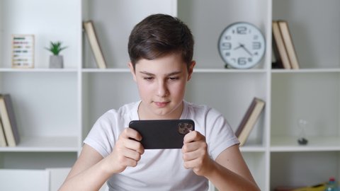 Beautiful boy 13 years old playing mobile game on smartphone at home. Teenager playing mobile phone. Kid using phone for gaming. Child playing video game indoors