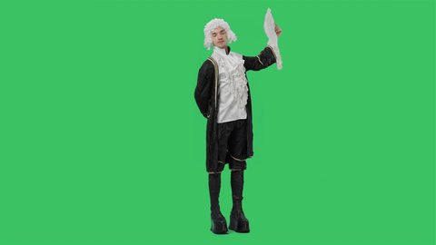 Portrait of courtier gentleman in black historical vintage suit and white wig, waving a fan, bowing and curtsy. Young man posing in studio with green screen background. Full lenght. Slow motion.