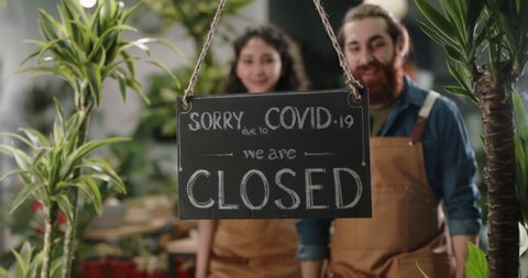 Positive employees reopening flower shop after COVID-19 pandemic. Happy greenhouse workers hanging open again sign at door - small business people after quarantine 4k footage