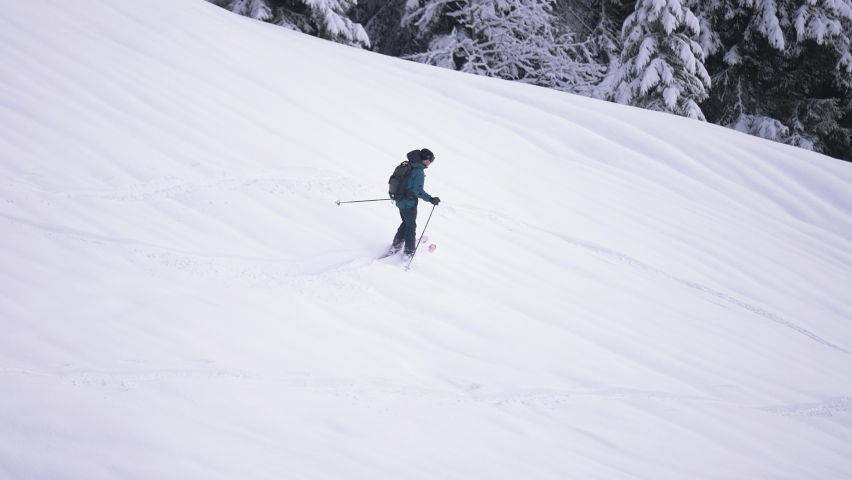 Action tracking view of man skiing down snowy mountain in slow mo