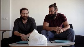 Video of two happy friends taking out a dürum kebab from the delivery bag at home, on the living room while sitting on the sofa