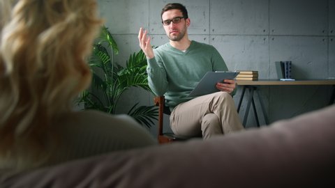 A young professional psychotherapist explaining to a patient the causes of depression. Young man with clipboard at psychotherapy