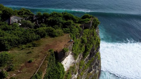 Man sits on the end of cliff above ocean on Uluwatu cliff Bali Indonesia. High quality 4k aerial epic footage