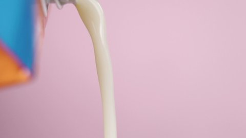 Pouring vegetable oat milk from a pack in slow motion. Macro shot. On a colored pink background. Alternative nutritional product without lactose.