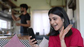 Beautiful Asian Woman making a video call smiling and talking with her friend while man work hard in modern kitchen.Businesswoman having video call discussing,working online meeting with team at home.