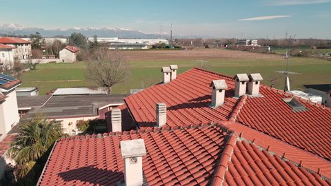 Tiled Roof Houses With Chimneys And Antennas With Meadows And Mountains In Background - aerial sideways