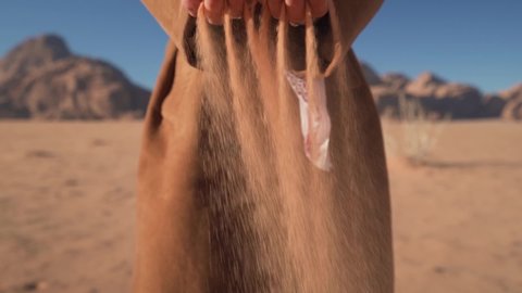 Cinematic slow motion close-up of sand falling from hands and a face of a pretty white woman tourist dressed as a local Bedouin wearing a keffiyeh in the Wadi Rum desert in Jordan on a clear sunny day