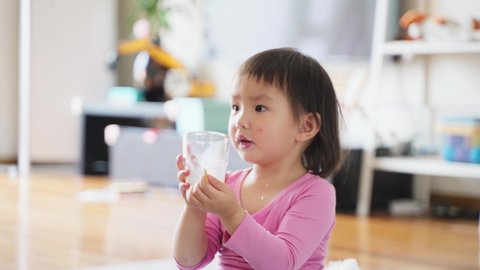 close up of lovely asian baby girl holding glass of milk drinking at home baby growth concept