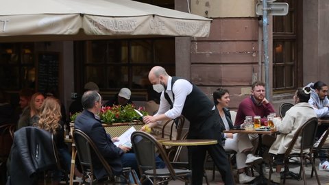 Strasbourg, France - May 19, 2021: Waiter serving clients at the table on pedestrian district as bars and restaurants reopen after two months of nationwide coronavirus outbreak