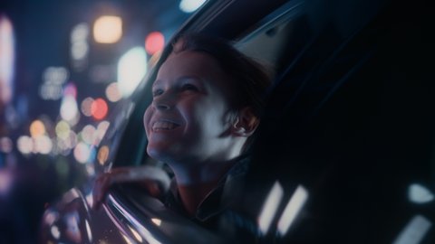 Excited Young Boy is Sitting on Backseat of a Car, Commuting Home at Night. Looking Out of the Window with Amazement of How Beautiful is the City Street with Working Neon Signs. Cinematic Footage.
