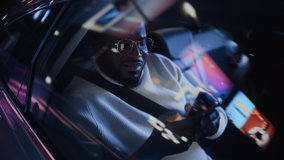 Stylish Black Man in Glasses is Commuting Home in a Backseat of a Taxi at Night. Handsome Male Using Smartphone and Looking Out of Window while in a Car in Urban City Street with Working Neon Signs. - Powered by Shutterstock - Get 15% off with code: PIKWIZARD15