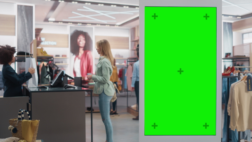 Customer Using Floor-Standing Touch Display with Green Screen Chroma Key Mock-Upf while Shopping in Clothing Store. She is Checking for Information, Looking at a Floor Plan, Choosing Items Online.