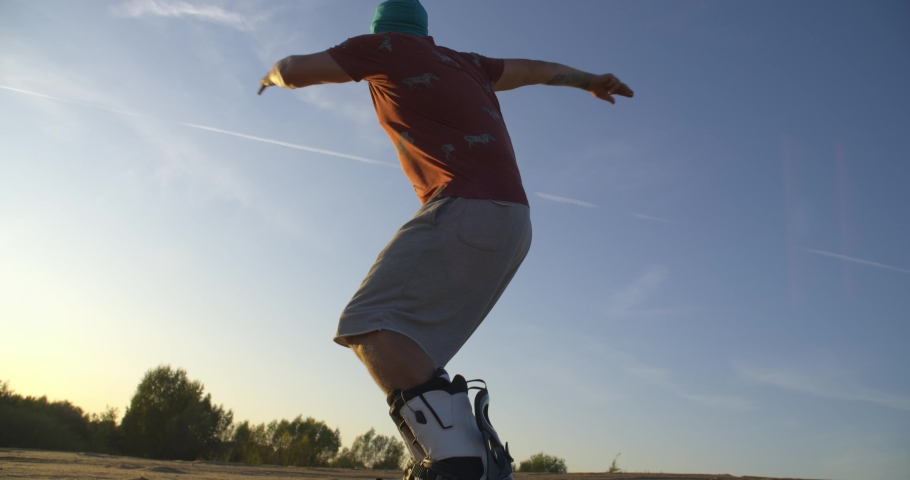 SLOW MOTION hipster man athlete in shorts tries doing tricks with a Board on sand dunes. Sandboard, snowboard, sunset, desert, flare