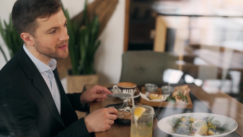 Cute stylish man enjoys a salad sitting in a restaurant by the window