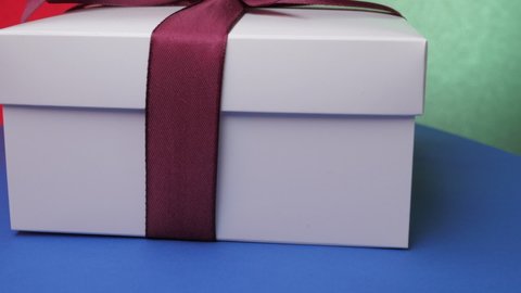 Decorative anniversary present box with purple ribbon and bow on blue table against green and red wall zoom out. Concept celebration