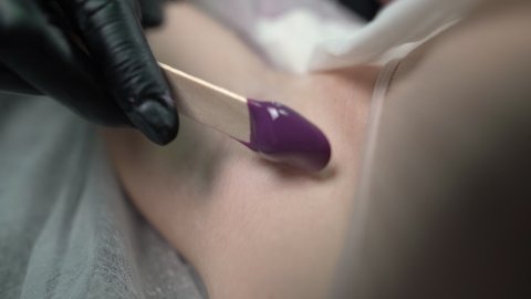 A master cosmetologist performs a procedure for removing hair from the armpits of a young woman using a shugaring paste. Beauty and body care concept. Close-up.