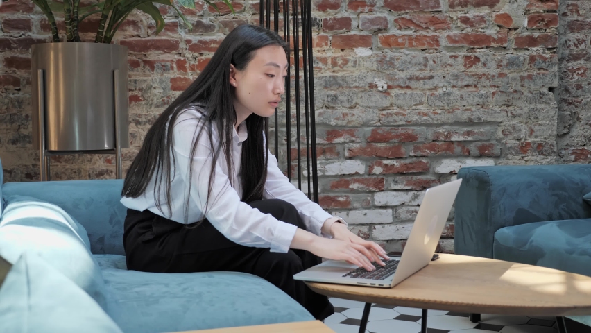 Oh no. Stressed chinese sad businesswoman sitting on the couch working on laptop while having feeling headache looking frustrated thinking of money debt, budget loss, bankruptcy in loft office. Royalty-Free Stock Footage #1072803167