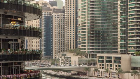 Dubai Marina waterfront with towers and bridge near restaurants from shoping mall balcony in Dubai day to night transition aerial timelapse, United Arab Emirates.