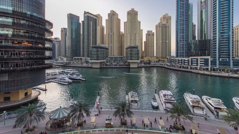 Dubai Marina waterfront with towers and yachts near restaurants from shoping mall balcony in Dubai day to night transition aerial timelapse, United Arab Emirates.