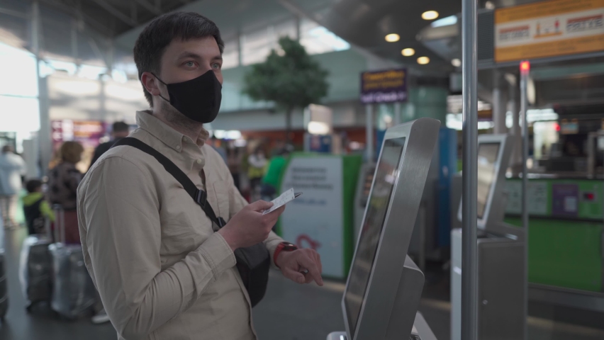 Passenger in mask self-check-in baggage for flight in machine in terminal, travel safety concept, new normal, social distance during coronavirus outbreak. Man use self service check in at airport | Shutterstock HD Video #1072822568