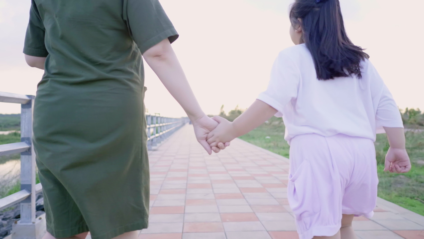 Back view of Asian mom and kid holding hand and running outdoor on track in the evening to watch the sunset, spending time together, Mom and daughter concept