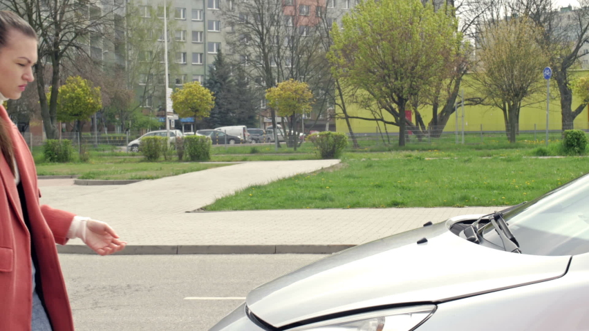 Young woman using smartphone, calling for assistance or tow truck while standing near her car with open hood on the road side.