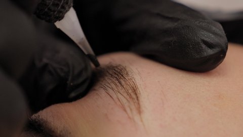 Close-up of a beautician doing permanent eyebrow makeup for a young woman.
