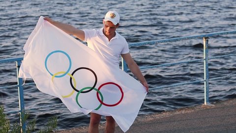 Ulyanovsk. Russia. 05.19.21. Athlete with the Olympic flag in his hands on the banks of the Volga at sunset. Olympic Games 2022 in Beijing. Olympic games and the 2022 olympic flag.