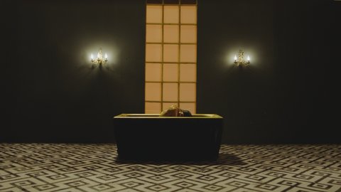 Sexy stylish woman on bikini and with shining glitters in her beautiful body sitting and moving inside golden bathtub in slow motion. Girl lying inside water in bathroom .