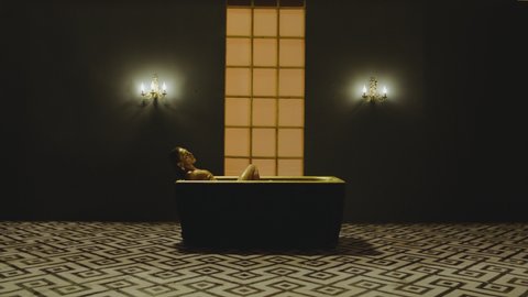 Sexy stylish woman on bikini and with shining glitters in her beautiful body sitting and moving inside golden bathtub in slow motion. Girl lying inside water in bathroom .
