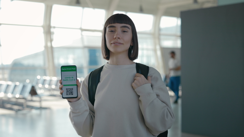 Portrait of charming lady holding modern smartphone with certificate with immunity for Covid-19 on screen. Female tourist with backpack using digital green pass while travelling abroad. Royalty-Free Stock Footage #1072843901