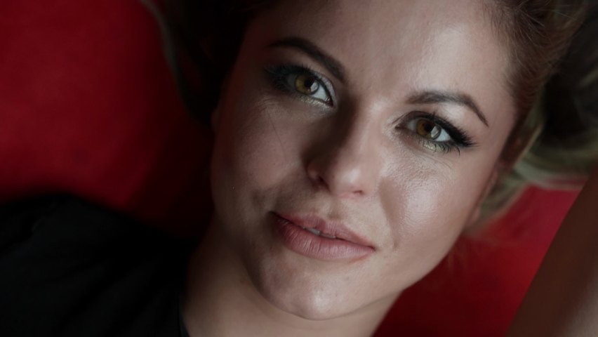 excited beautiful woman is laying on red linen, closeup view of face, touching lips by fingers passionately