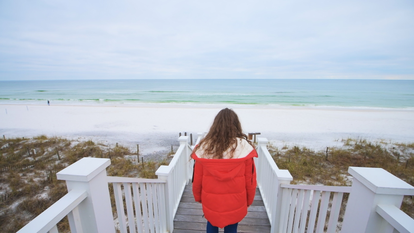 Point of view pov handheld walking behind young woman down stairs of wooden pavilion gazebo boardwalk by sea sand ocean beach at Gulf of Mexico at Seaside, Florida