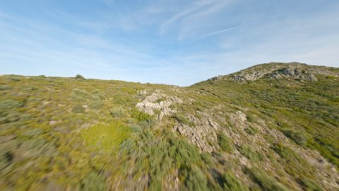 View from above, flying at high speed over a mountain range covered by a green vegetation with the mediterranean sea in the distance. Sardinia, Italy. Drone point of view, mountain surfing.