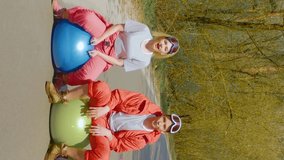 Vertical video of happy friends in bright ski suits sings fun on bright balls on a forest road in sunny weather. Young people musicians in goggles with colorful balls in the forest