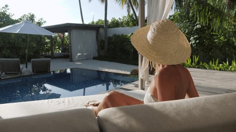Young woman relaxing by the pool in her private beach villa. Female living luxury lifestyle in a beach resort surrounded by lush green garden 