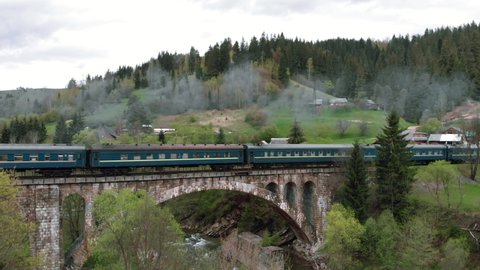 Passenger train passing over viaduct bridge in mountains landscape. Electric train crossing old railroad bridge. Passenger train moving on railway bridge