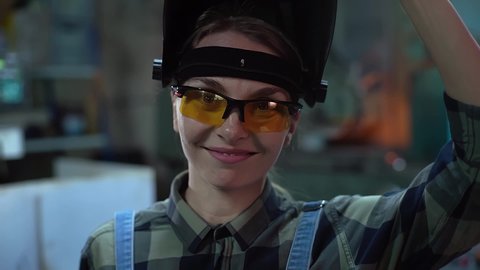 The female welder takes off her mask and smiles